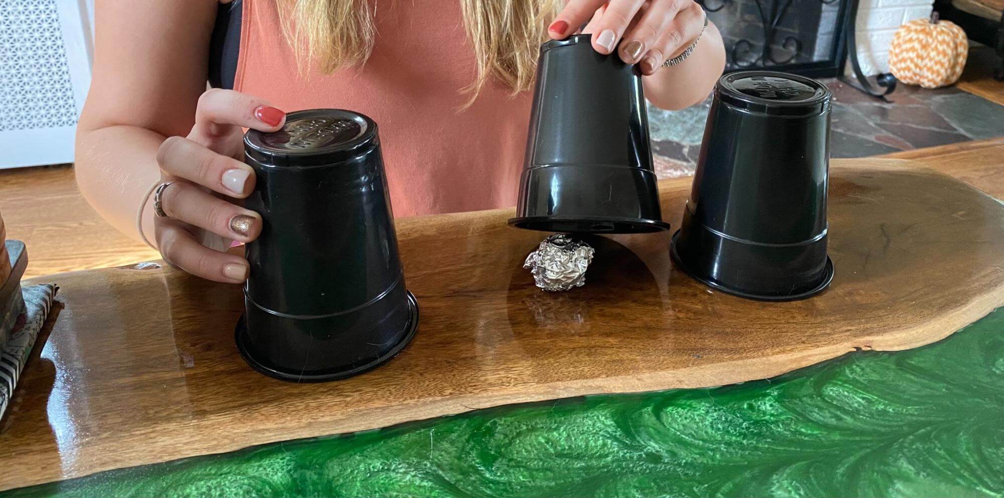 woman holding cups with an aluminum ball under one of them